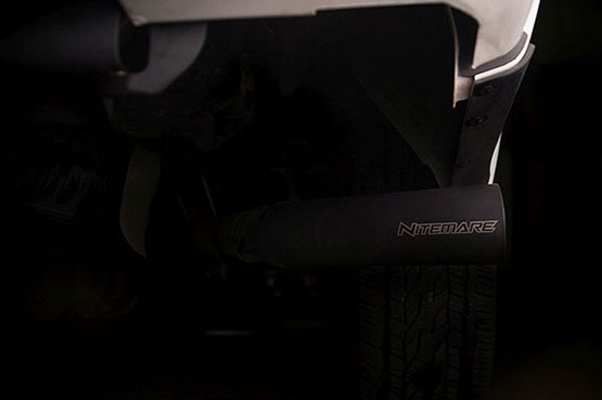 Close-up of a black exhaust tip labeled "Nitemare" on the ROUSH F-150 Nitemare, with a treaded tire in the background, showcasing the 600 horsepower beast—renowned as the Fastest Factory Street Truck.