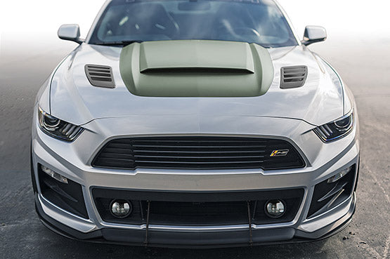 The silver sports car, boasting a 727-horsepower engine, features a prominent hood vent and aggressive front design, echoing the fierce spirit of a muscle car. Parked on the road, it stands as a testament to power and style.