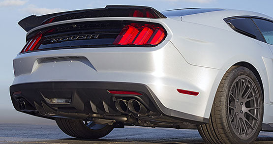 Rear view of a silver ROUSH P-51 sports car, showcasing dual exhausts, a black spoiler, and red taillights—a true muscle car with its 727-horsepower engine.