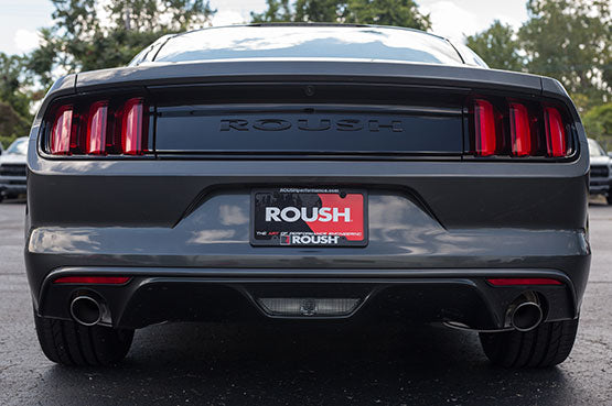Rear view of a dark gray ROUSHcharged Mustang parked on asphalt, featuring distinctive taillights and a dual exhaust system, embodying the power of its 670-horsepower ROUSH Stage 3 engine.