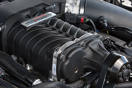 Close-up of a ROUSH Stage 3 supercharger in an engine bay, showcasing its belts, pulleys, and surrounding components. This ROUSHcharged Mustang powerhouse produces an astounding 670-horsepower.