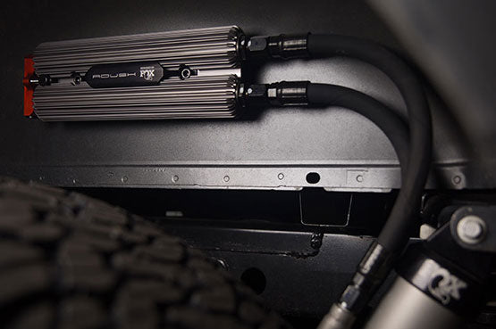 Close-up of a metal dual reservoir system, perfectly integrated into the Off-Road Suspension of a ROUSH Raptor, with two connected hoses visible.