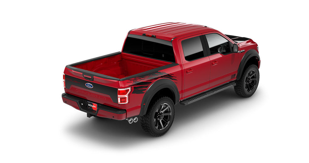 The ROUSH F-150, a red pickup truck with black graphics, is seen from the rear right angle. It boasts a double cab and spacious open cargo bed, enhanced by its Fox 2.0 suspension system and robust all-terrain tires.
