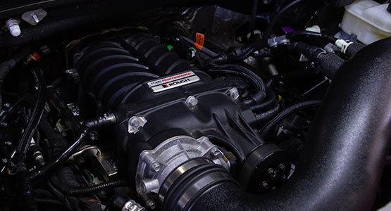 Close-up of an engine with a visible ROUSH F-150 SC supercharger, surrounded by various wires and components in a dark engine bay, showcasing the power of its performance exhaust system.