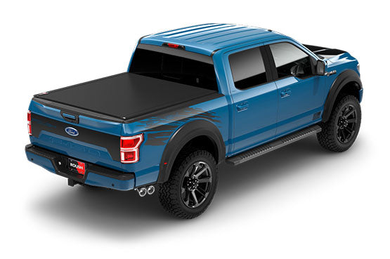 A blue F-150 pickup truck with a covered bed and black wheels is shown from a rear angle, showcasing its off-road capability.