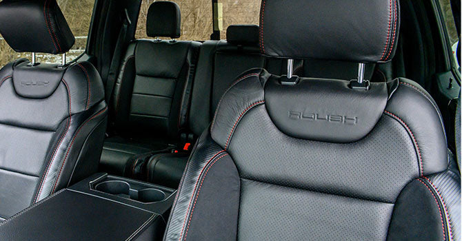 Black leather car seats with red stitching are showcased in the interior of a ROUSH Raptor, featuring embossed logos on the headrests.