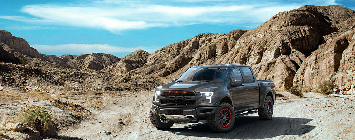 A black ROUSH Raptor performance truck navigates the rocky desert landscape under a blue sky, showcasing its off-road capable prowess.