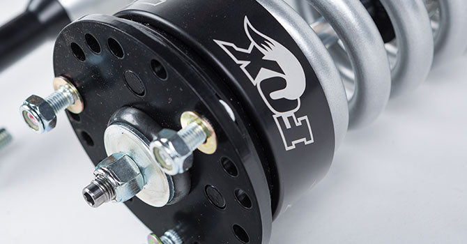 Close-up of a suspension coilover with a black top mount, featuring the FOX logo, engineered to enhance the ROUSH F-150's off-road capability.
