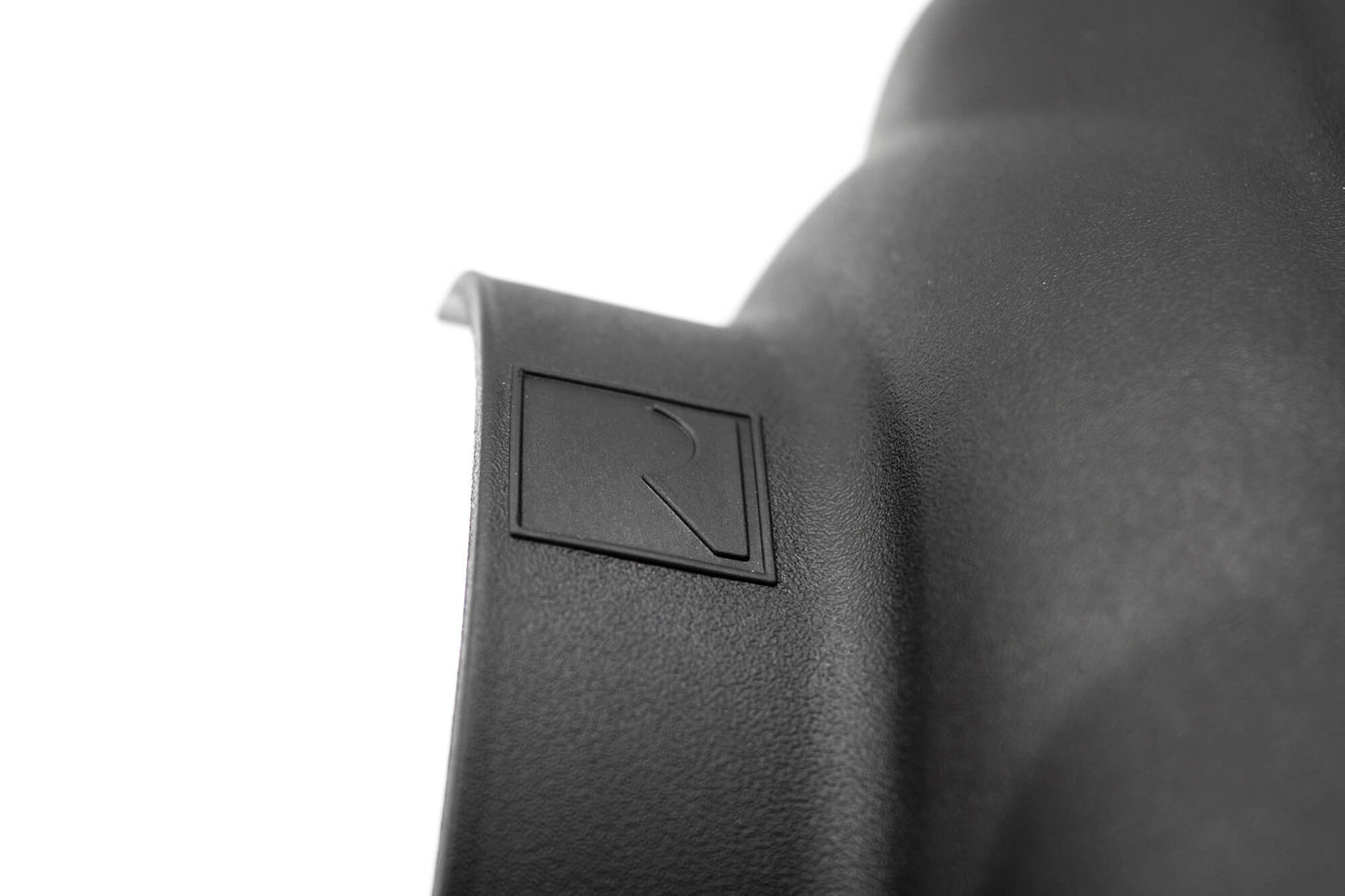 Close-up of a black textured surface showcasing a raised square logo with an embossed "R" on a curved edge, reminiscent of the enhanced power seen in the Mustang 5.0L V8 with Roush Performance Air Intake.
