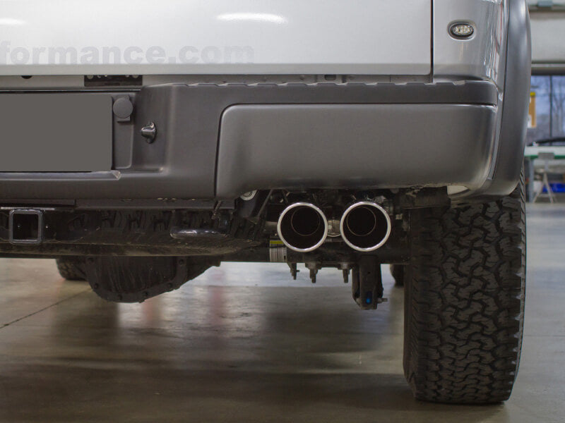 Close-up of a vehicle's rear showcasing dual stainless steel exhaust pipes and a portion of the bumper in a garage setting, hinting at the enhanced horsepower and torque it delivers.