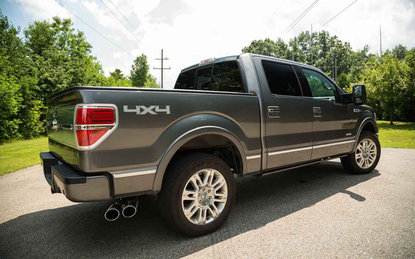 A gray 4x4 pickup truck, equipped with a robust F-150 exhaust system, is parked on a road, surrounded by trees under a clear sky.