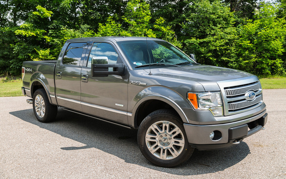 A gray Ford F-150 pickup truck, equipped with a Roush exhaust system, is parked on a paved surface with green trees in the background.