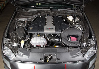 A Mustang 5.0L engine showcases its visible components and a striking 5.0 emblem under the hood, complete with a Cold Air Kit for enhanced air intake efficiency.