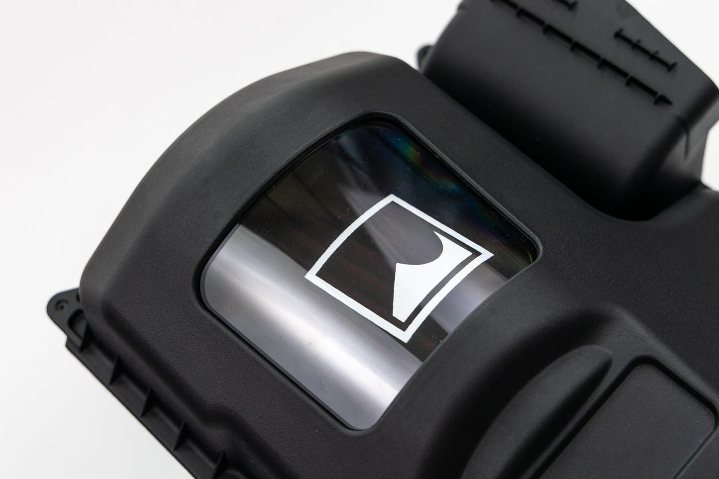 Close-up of a black electronic device with a shielded cover featuring a logo on a small transparent window. The device has a smooth and contoured surface with prominent ridges and a clasp, reminiscent of the rugged design you'd expect from the Roush Bronco Air Induction System built for off-road racing.