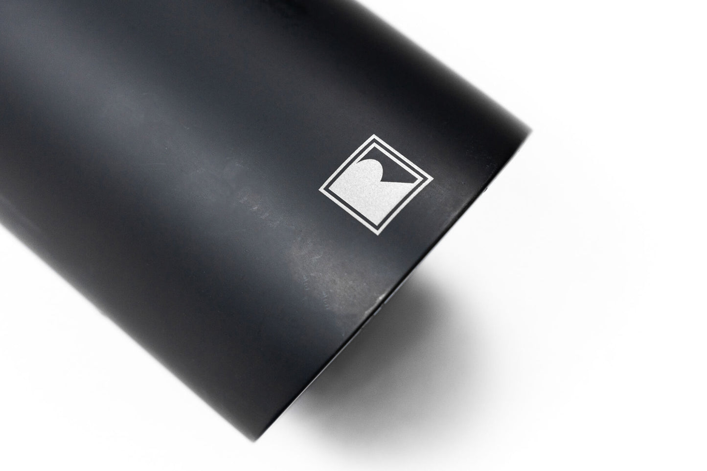 A black cylindrical object with a white logo featuring a stylized "R" inside a square. Specifically designed for the 2021-2024 Ford Broncos, this component ensures improved clearance and departure angle for rugged terrains. The background is white.