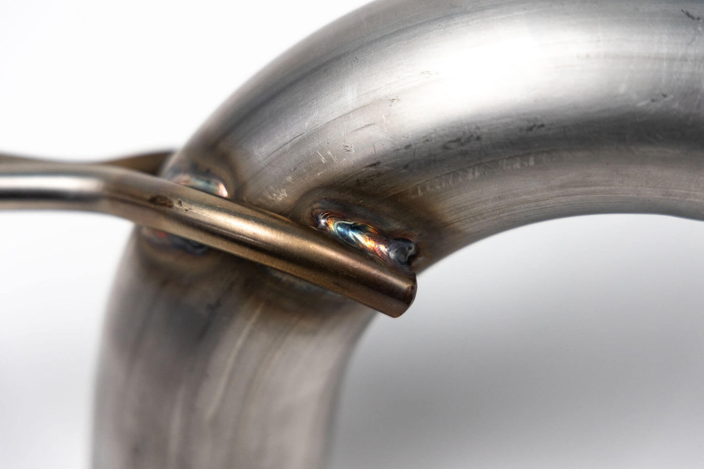 Close-up of a welded metallic joint where two cylindrical metal pieces intersect and are joined by welding, showing some discoloration around the weld area. Ideal for enthusiasts upgrading their 2021-2024 Ford Broncos with the Roush Bronco Axle-Back Exhaust to achieve improved clearance and departure angle.