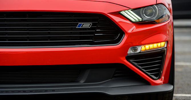 Close-up of a ROUSH Mustang front, highlighting the performance-inspired grille, headlight, and indicator light.