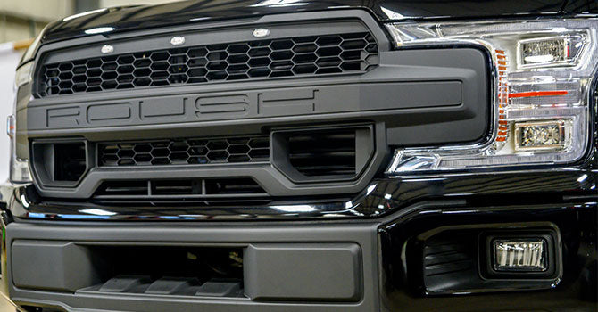 Close-up of a black Roush Nitemare truck grille with bold lettering, highlighting the front headlight design and vent details, powered by a supercharged 650-horsepower V8 engine.