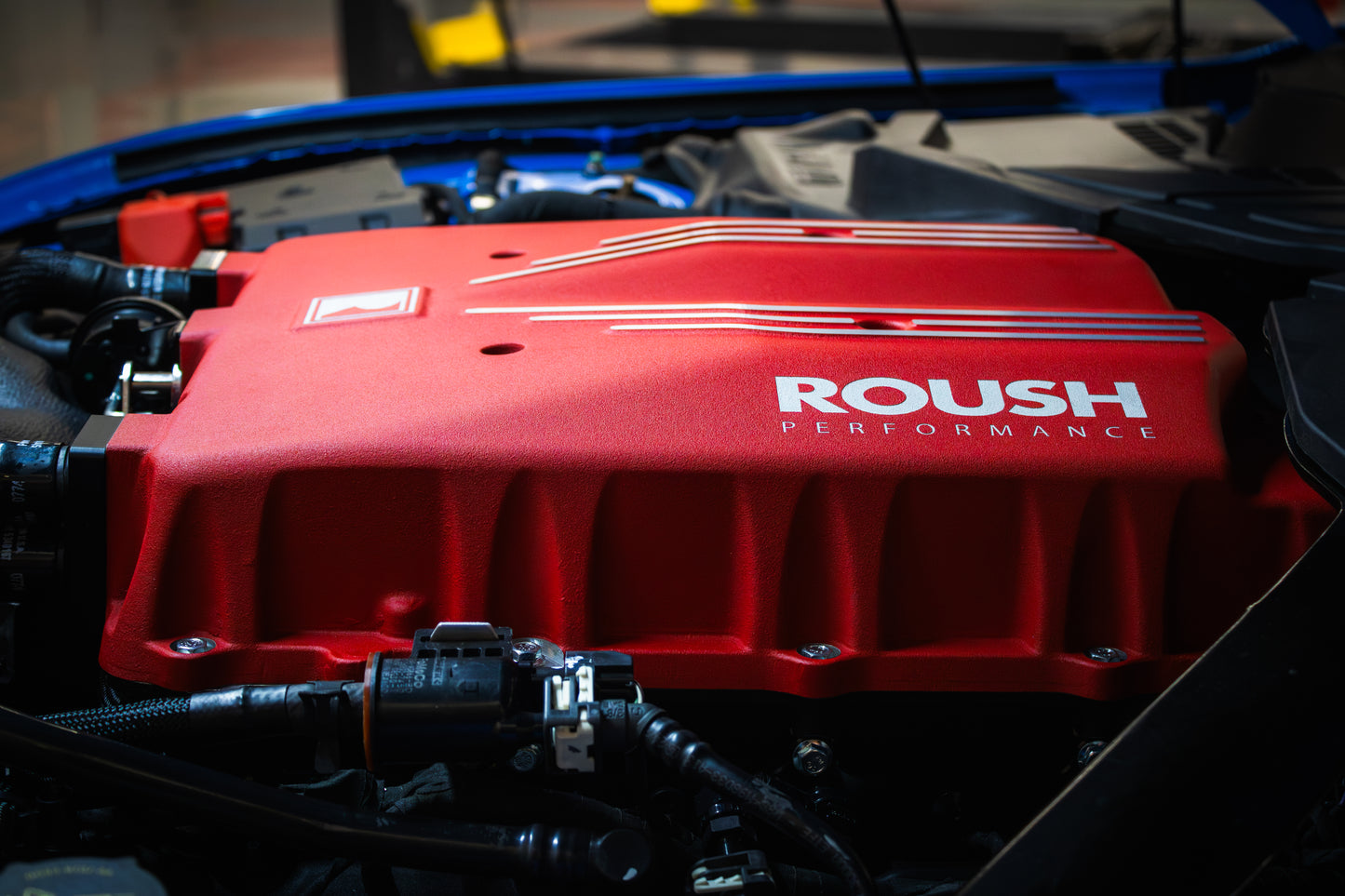 Close-up of a car engine with a bright red cover labeled "Roush Performance," featuring the powerful TVS R2650 Supercharger.