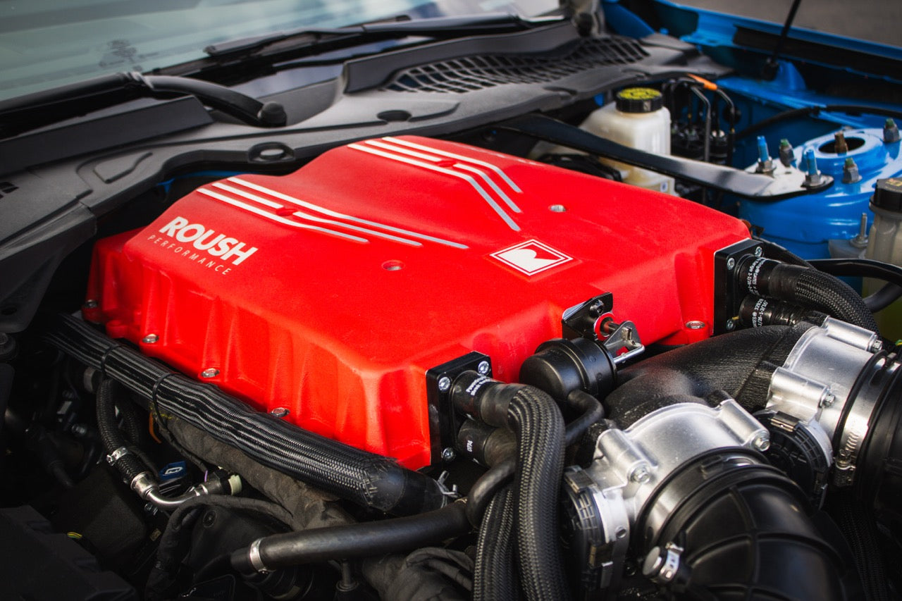A car engine with a prominent red Roush Performance cover and visible tubing, enhanced by the Supercharger Kit, hints at the power synonymous with the Roush S650 Mustang, boasting an impressive 740 horsepower.
