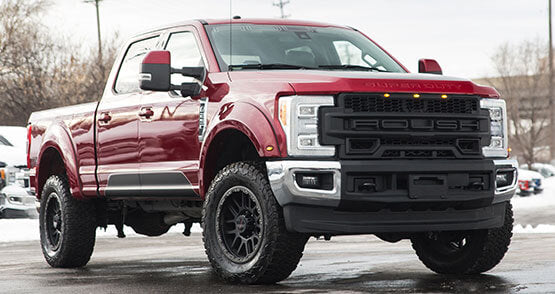 
                  
                    A red ROUSH Super Duty pickup truck, boasting rugged tires and a bold grille, showcases impressive towing capabilities as it stands proudly on a cloudy day.
                  
                