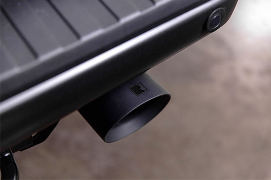 
                  
                    Close-up of a sleek black exhaust pipe, part of the ROUSH Raptor's Axle-Back Exhaust system, partially visible against a blurred background.
                  
                