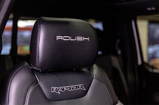 
                  
                    Close-up of a black car seat headrest with "ROUSH Raptor" embroidered at the top and "RAPTOR" on the main seat, embodying a rugged style akin to off-road wheels.
                  
                
