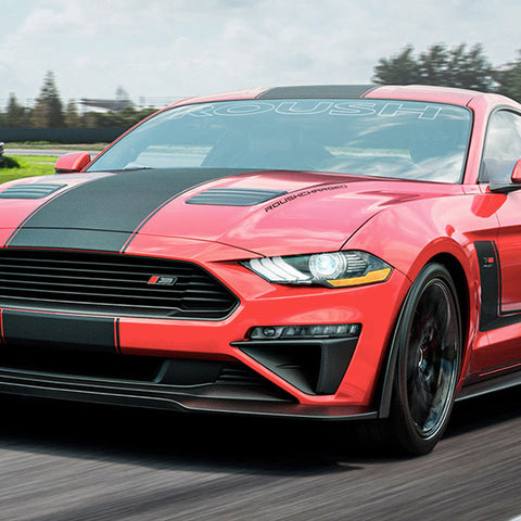 A red sports car with black racing stripes, equipped with an active exhaust system, roars through the racetrack.