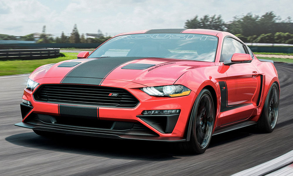 A red sports car with black racing stripes, equipped with an active exhaust system, roars through the racetrack.
