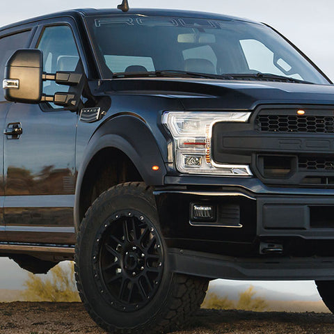 A black ROUSH F-150 pickup truck is parked outdoors, viewed from the front side, with rugged tires and reflective surfaces glistening under a cloudy sky. This 5.11 Tactical Edition is built for off-road performance.