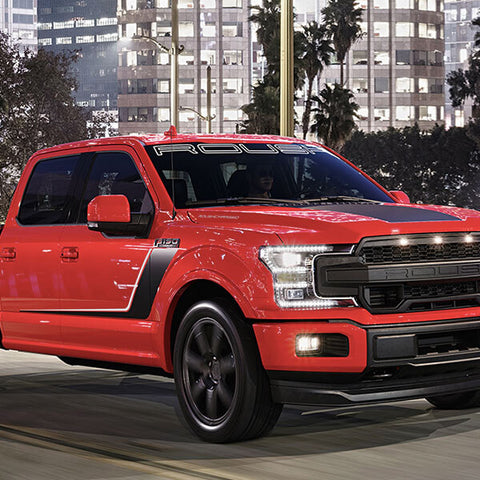 A red pickup truck, equipped with a supercharged 650-horsepower V8, cruises down a city street at night, with buildings and palm trees silhouetted in the background.