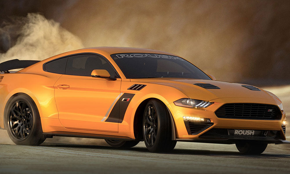 The ROUSH Stage 3 orange sports car, equipped with a supercharger and MagneRide suspension, effortlessly drifts on the sandy surface, creating an impressive dust cloud.