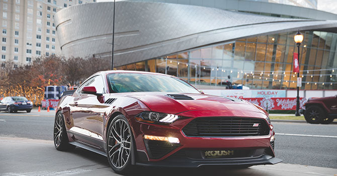 
                  
                    A ROUSH Mustang in striking red dominates the city street, poised elegantly in front of a modern, curved architectural building. This Jack Roush Edition is a true marvel, amplified by its powerful 775HP supercharger under the hood.
                  
                