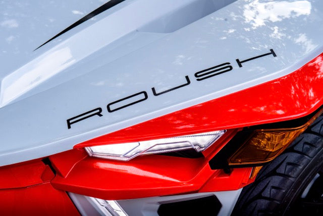 
                  
                    Close-up of a Slingshot Roush Edition’s front end featuring angular red and white body panels, a headlight, and the word "ROUSH" emblazoned above the light—showcasing its racetrack attitude.
                  
                