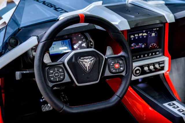 
                  
                    Close-up of a modern Slingshot Roush Edition dashboard featuring a steering wheel with controls, digital displays, and control buttons on a red and black interior for true racetrack attitude.
                  
                