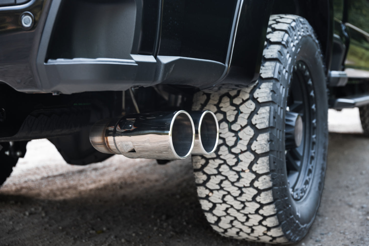 
                  
                    Close-up of a Roush Super Duty’s rear wheel with off-road tire and dual chrome exhaust pipes, parked on gravel—a bold stance powered by a turbodiesel V8 engine.
                  
                