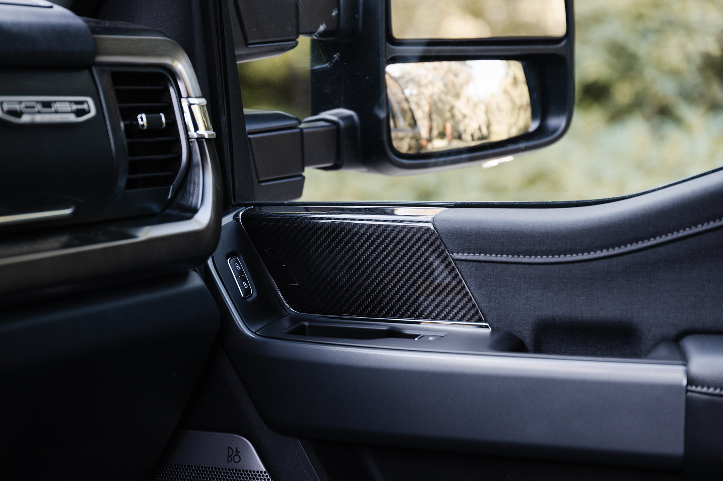 
                  
                    Close-up view of a Roush Super Duty car's interior showing the door panel, side mirror, window controls, and carbon fiber trim.
                  
                