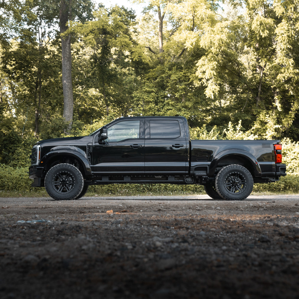 
                  
                    A black pickup truck with a turbodiesel V8 engine is parked on a gravel road, surrounded by dense green trees in the background.
                  
                
