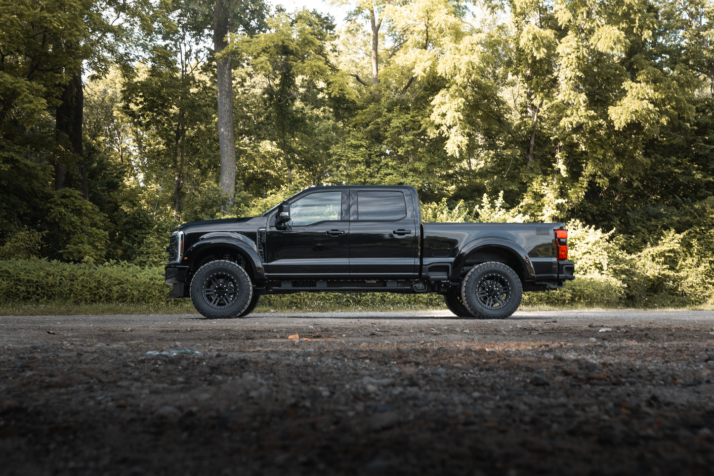 
                  
                    A black pickup truck with a turbodiesel V8 engine is parked on a gravel road, surrounded by dense green trees in the background.
                  
                