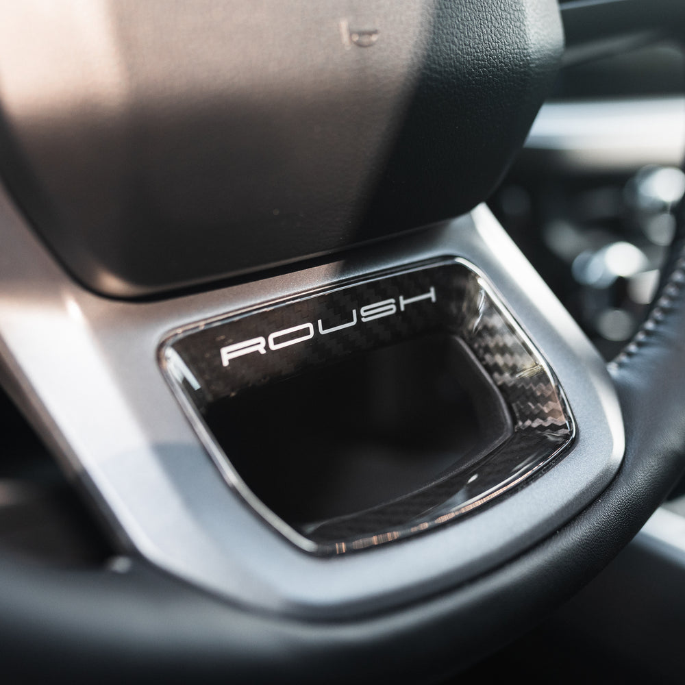 
                  
                    Close-up of a car steering wheel featuring the "ROUSH" logo on a metallic accent below the central hub, hinting at the impressive Roush Super Duty’s performance suspension.
                  
                