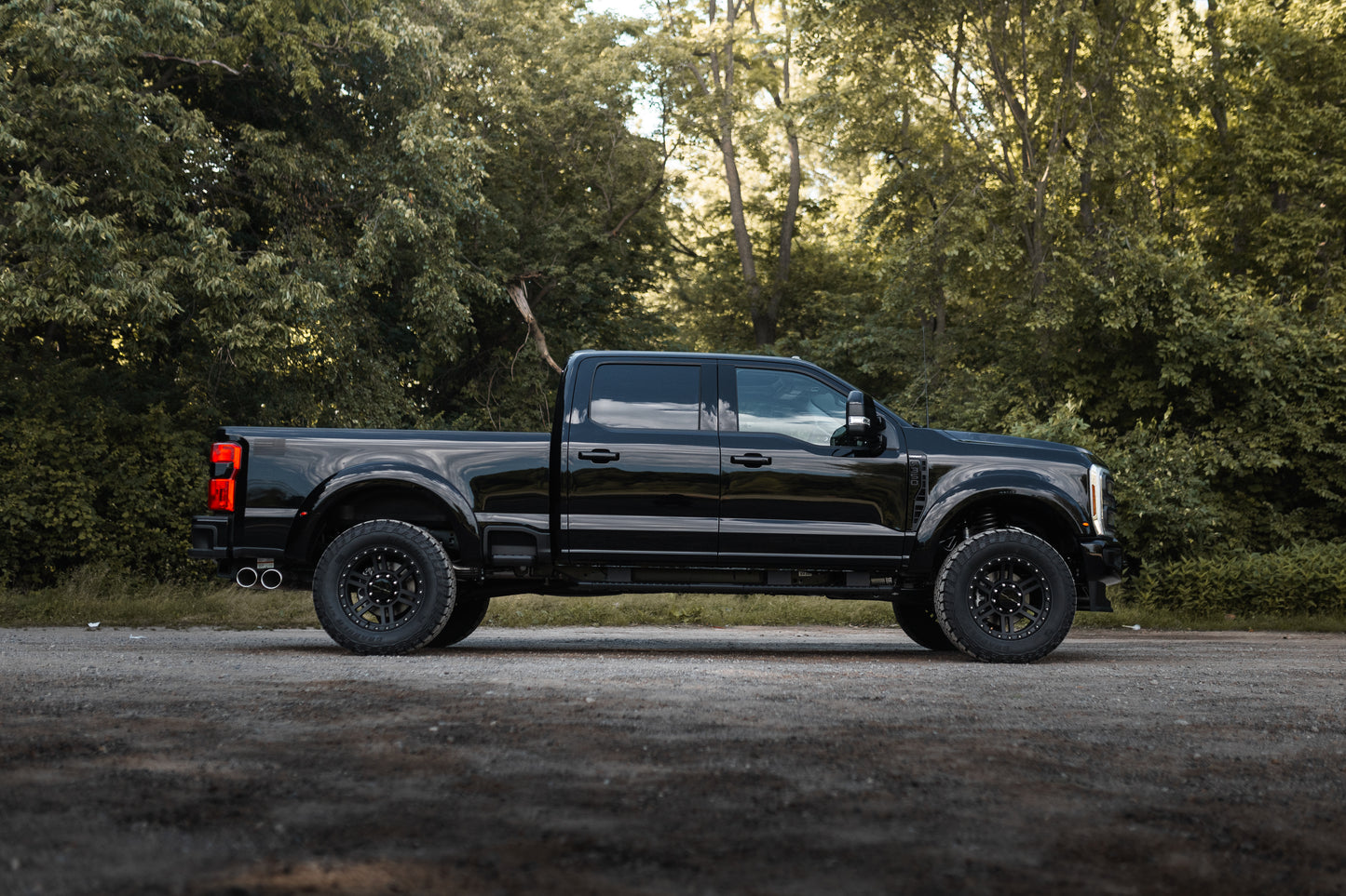 
                  
                    A black Roush Super Duty pickup truck with performance suspension is parked on a gravel surface, set against a backdrop of dense green trees and foliage.
                  
                