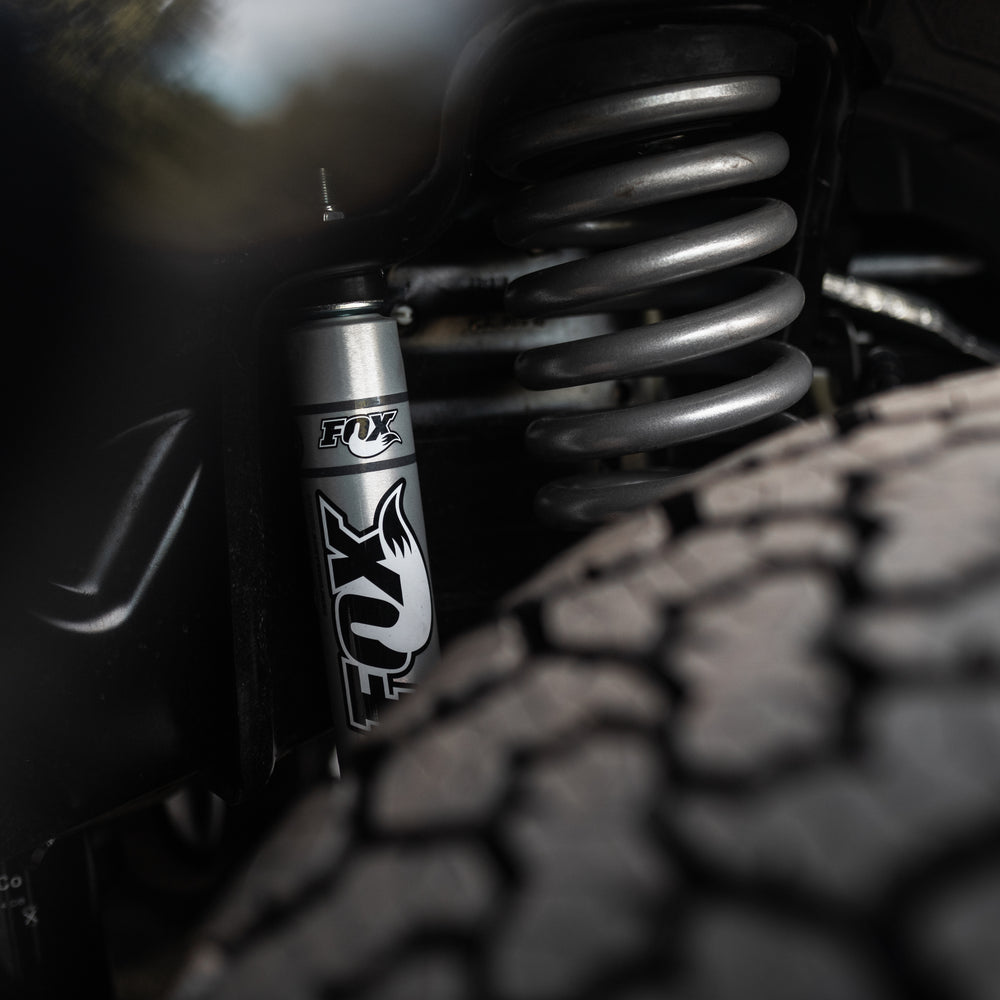
                  
                    Close-up of a Roush Super Duty's performance suspension system, featuring a Fox shock absorber, coiled spring, and textured tire.
                  
                