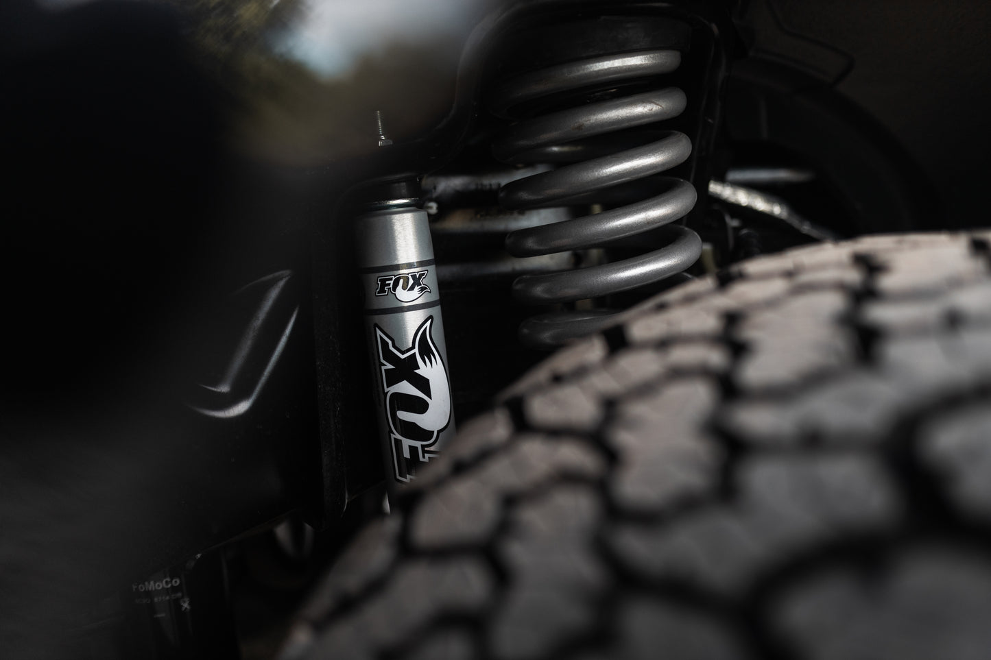 
                  
                    Close-up of a Roush Super Duty's performance suspension system, featuring a Fox shock absorber, coiled spring, and textured tire.
                  
                
