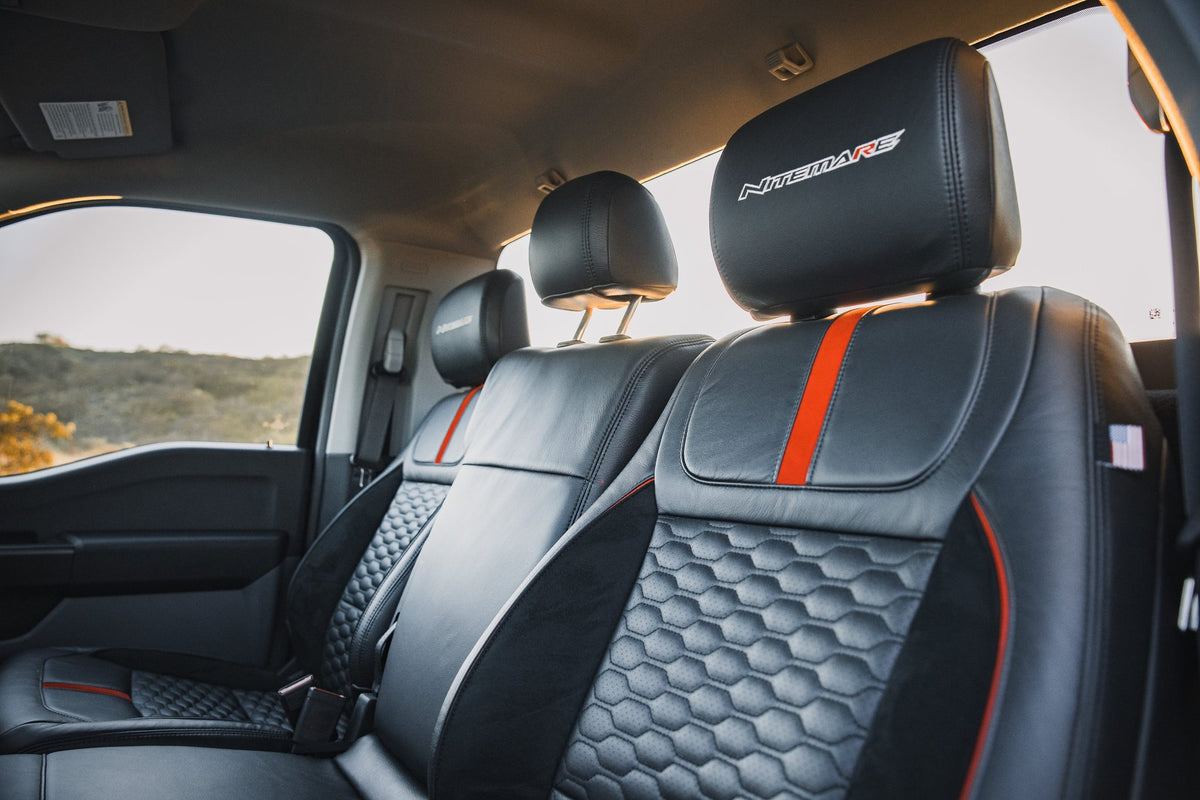 
                  
                    Interior of a Roush Nitemare F-150 cabin featuring black leather seats with hexagonal patterned inserts, red vertical accents, and “NITEMARE” embroidered on the headrests.
                  
                