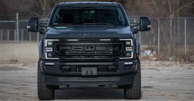 
                  
                    Front view of a black ROUSH Super Duty truck, featuring sleek 20-inch ROUSH wheels, parked in an outdoor area with a blurred fence and trees in the background.
                  
                