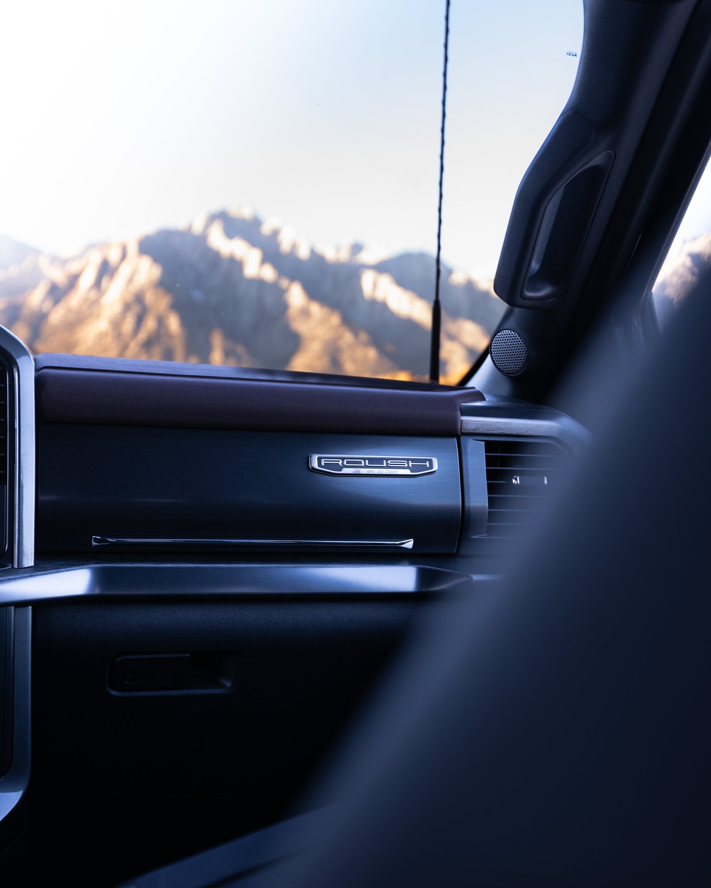 
                  
                    View from inside a 2023 Roush F-150 showing the dashboard and door, with mountains visible through the window in the background, highlighting Roush performance enhancements.
                  
                