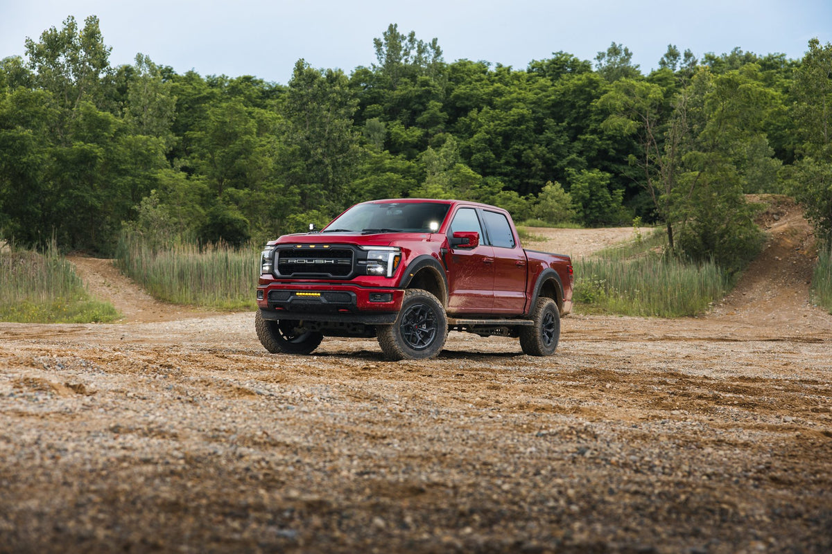 
                  
                    A red Roush RT6 F-150 truck with off-road performance styling parked on a gravel path in a wooded area.
                  
                