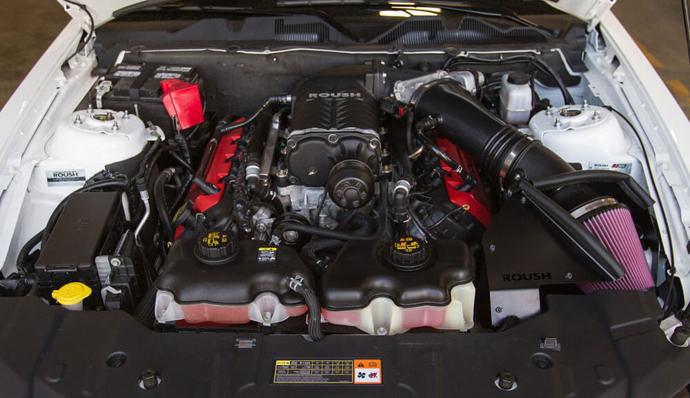 Close-up of a Roush engine inside a vehicle, featuring Eaton's TVS Technology with a black air filter, red valve covers, and various fluid reservoirs.