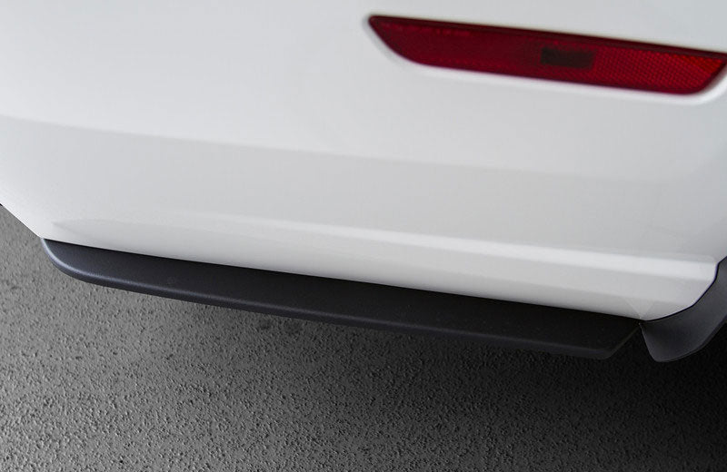 
                  
                    Close-up of the rear bumper and taillight of a white car, featuring part of the black lower trim with a Ford Mustang Rear Side Splitter and gray pavement visible.
                  
                