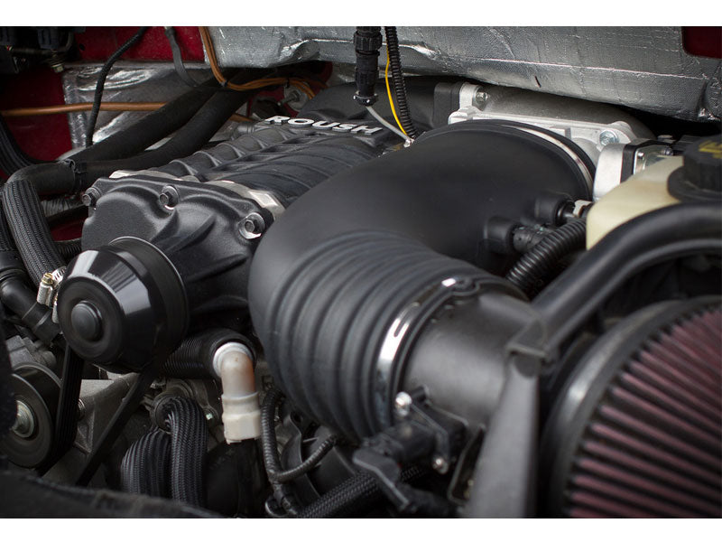 Close-up of a car engine showing a Roush R2300 performance modification with a prominent black intake featuring Eaton TVS Technology and various connectors.